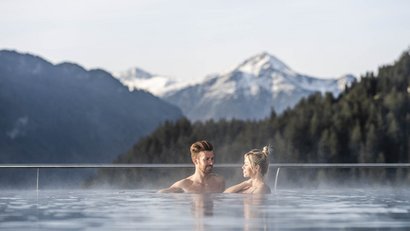 Paar entspannt im beheizten Außenpool mit Bergblick und Nebel