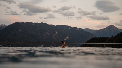 Frau entspannt im Infinity-Pool mit Bergblick bei Sonnenuntergang