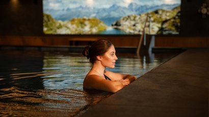 Frau entspannt im Hallenbad mit Berglandschaft im Hintergrund
