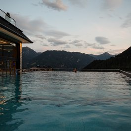 Infinity-Pool mit Bergblick bei Sonnenuntergang und Person im Wasser